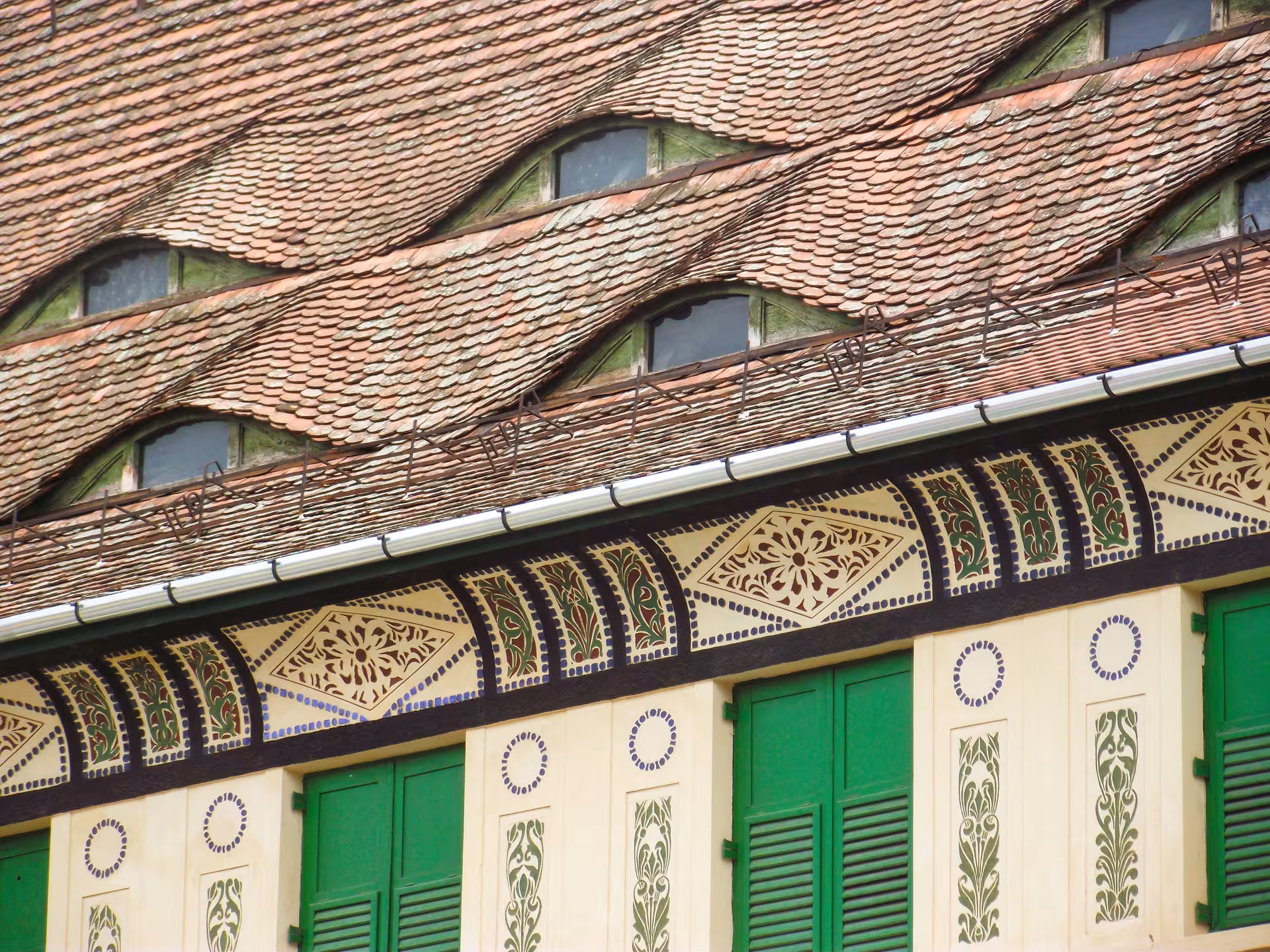 Ornate Romanian building facade with green shutters and decorative terracotta roof tiles in Sighisoara