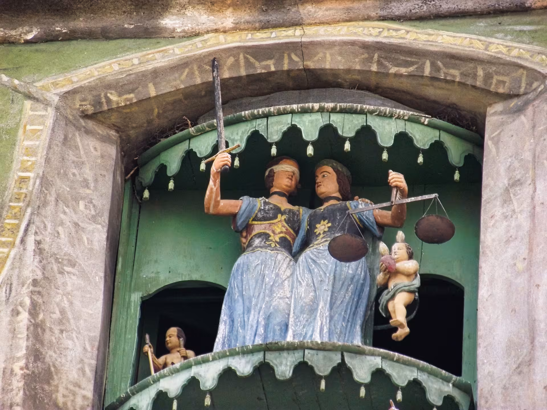 Ornate painted sculptures of Lady Justice with sword and scales on Sighisoara clock tower facade