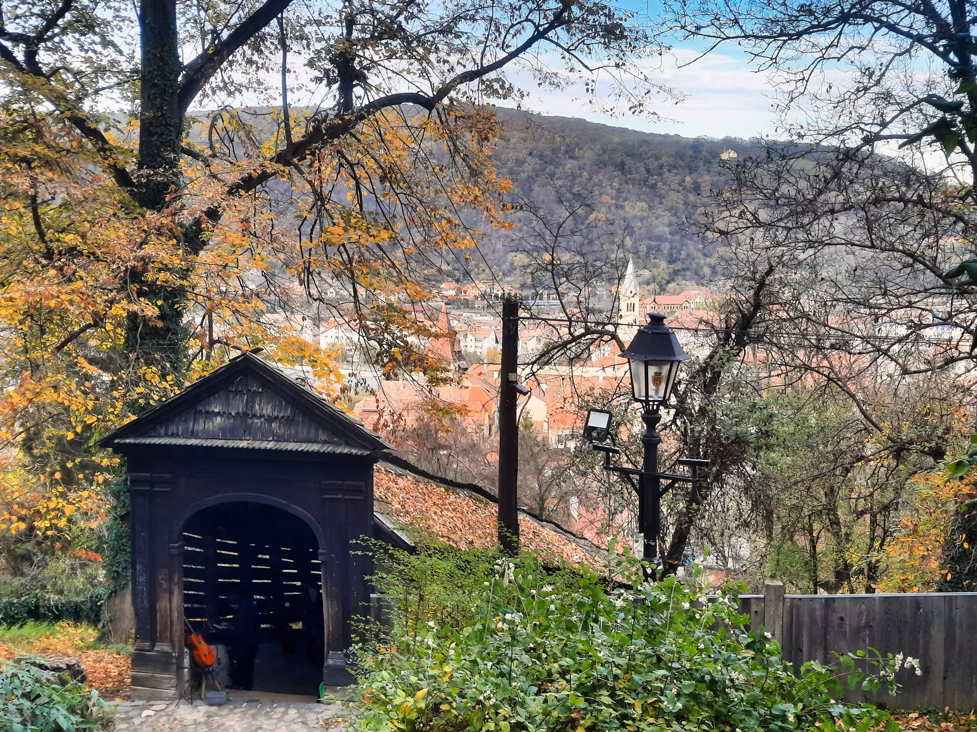 Panoramic view of Sighisoara old town with red rooftops, wooden shelter, lantern, and autumn trees on hillside