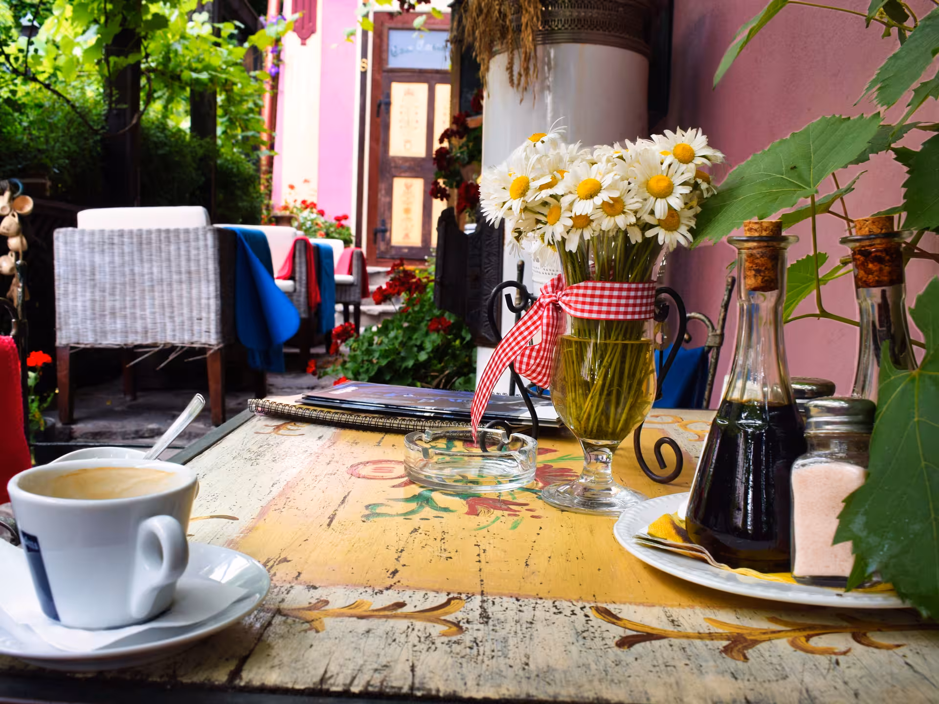 Charming outdoor café table in Sighișoara with coffee, daisies, and condiment bottles in a colorful courtyard