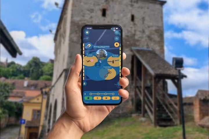 Hand holding smartphone with Sighisoara scavenger hunt app in front of Saxon Citadel tower