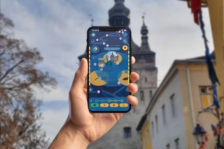 Hand holding smartphone with Sighisoara scavenger hunt game app, Saxon citadel clock tower in background