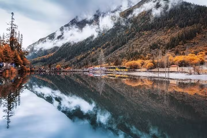Tranquil lake reflects autumnal trees and misty mountains in Bipenggou, offering a serene escape in nature.