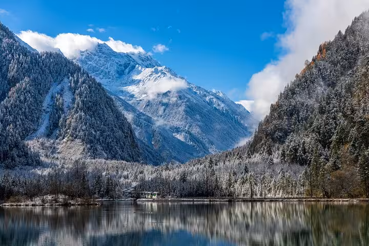 Snow-dusted Bipenggou Valley with a serene lake reflecting majestic mountains, ideal for nature exploration.