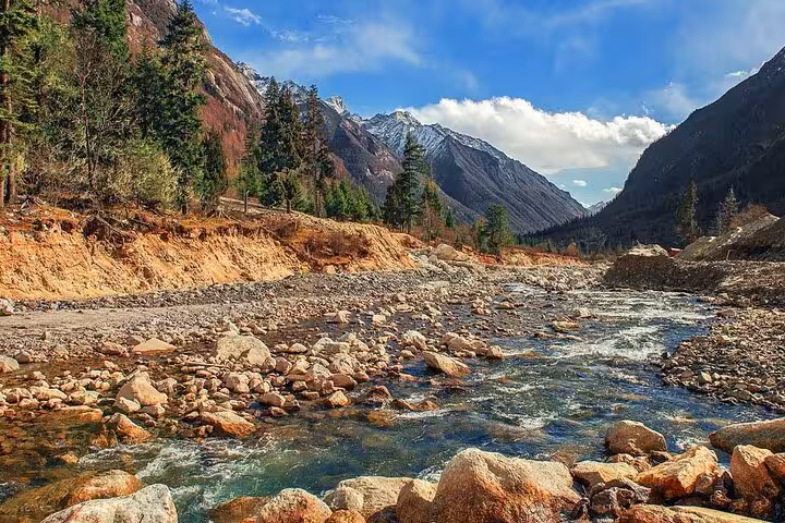 Pristine river flows through rocky terrain with lush forests and majestic mountains in the Bipenggou Valley.
