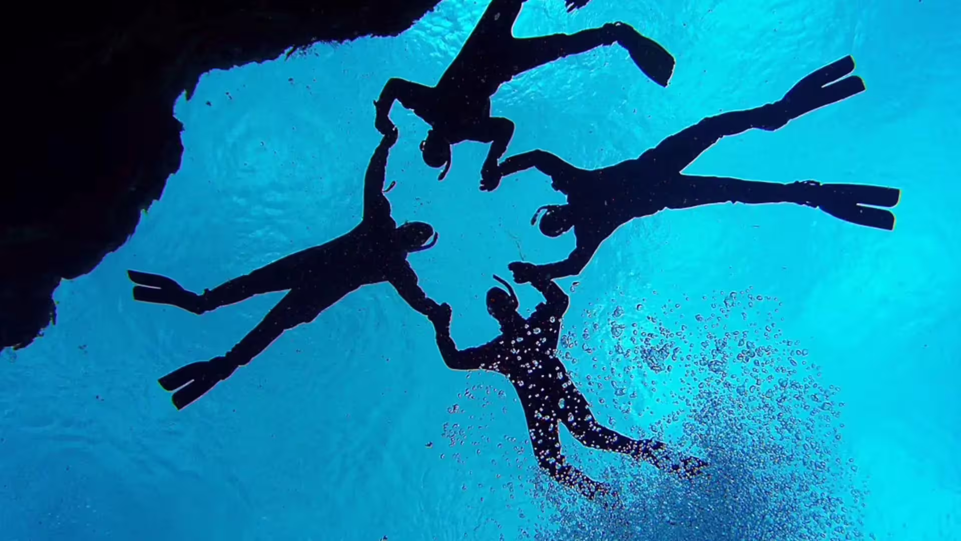 Silhouettes of scuba divers underwater in crystal clear blue water at Silfra, Iceland
