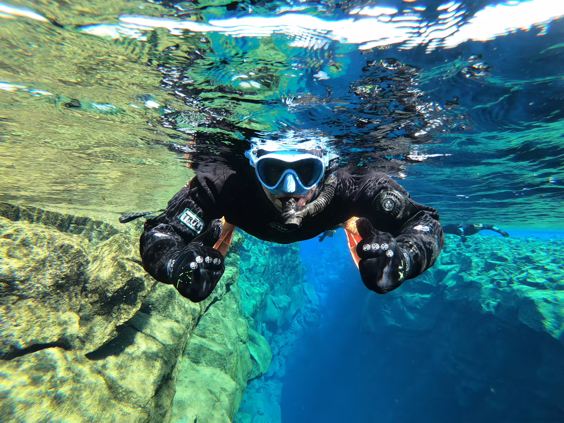 Snorkeler in black drysuit and blue mask diving through Silfra fissure crystal clear water Iceland