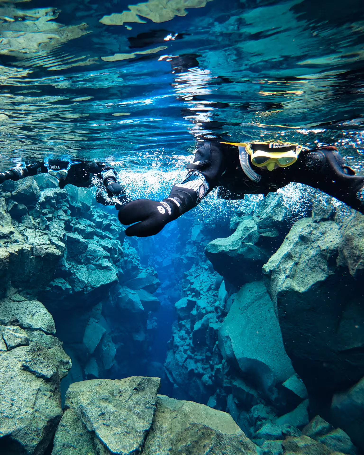 Snorkeler diving through Silfra fissure crack in crystal clear blue water, Thingvellir Iceland