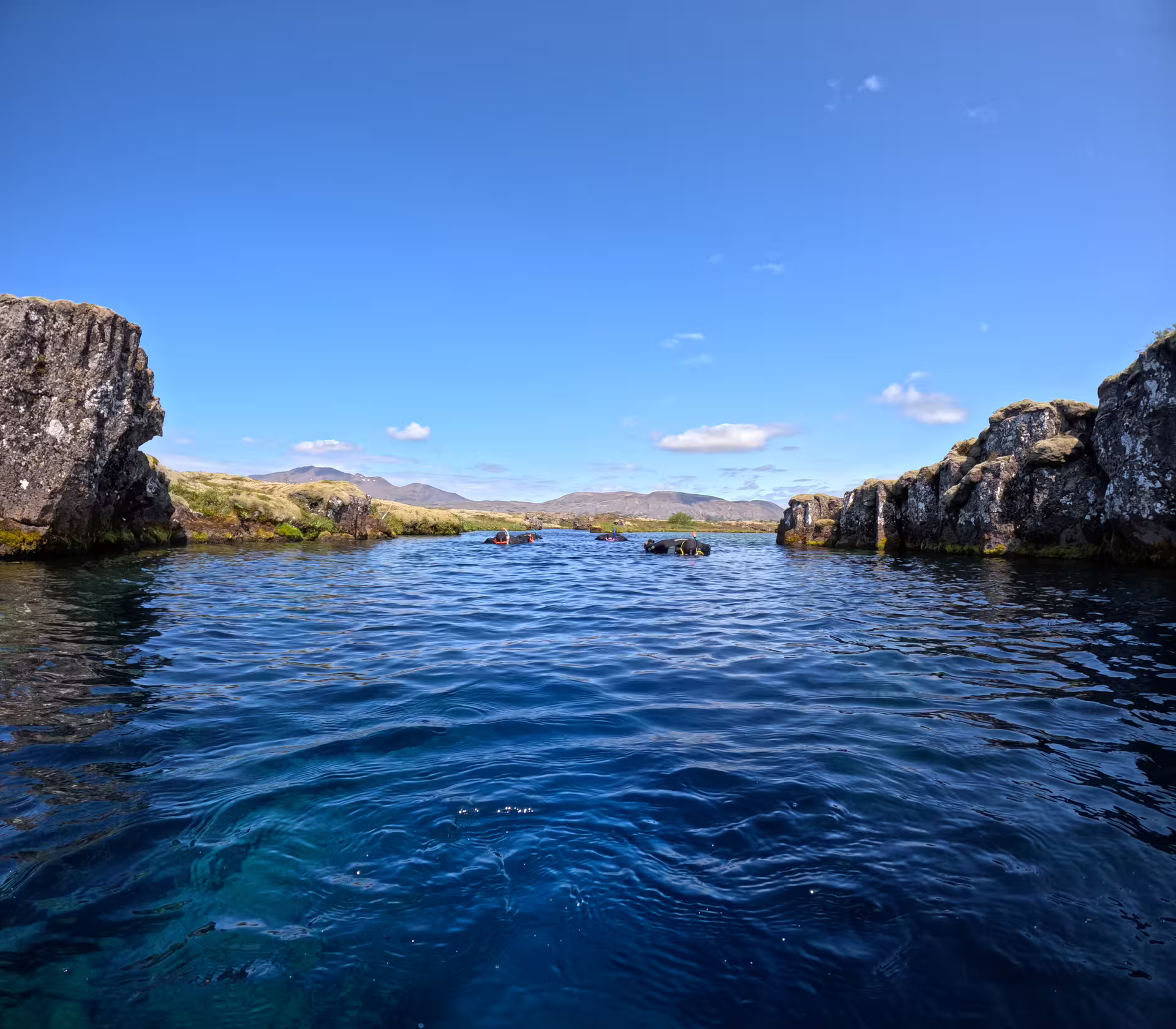 Snorkelers floating in the crystal-clear blue waters of Silfra fissure, Iceland, flanked by volcanic rock walls