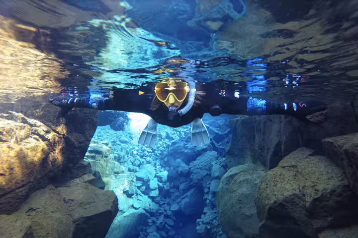 Snorkeler floating between tectonic plates in crystal clear blue waters of Silfra fissure, Iceland