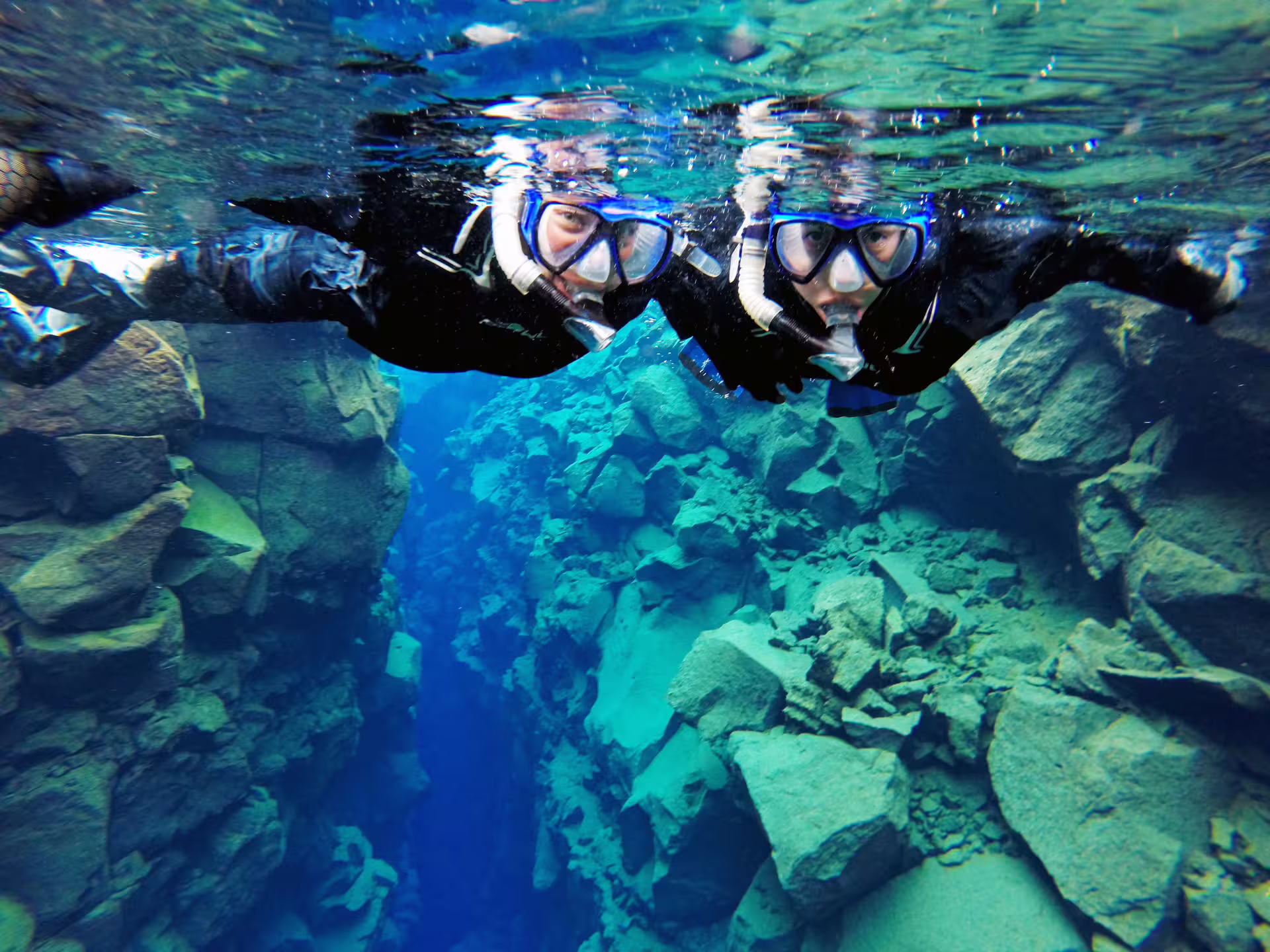 Snorkelers explore the crystal-clear waters of Silfra fissure, part of the Golden Circle tour, offering a unique underwater experience.