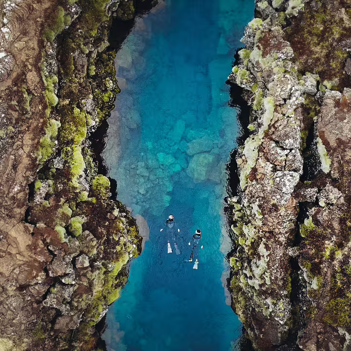 Snorkelers explore the crystal-clear waters of Silfra Fissure, Iceland, surrounded by stunning volcanic rock formations near Reykjavik.