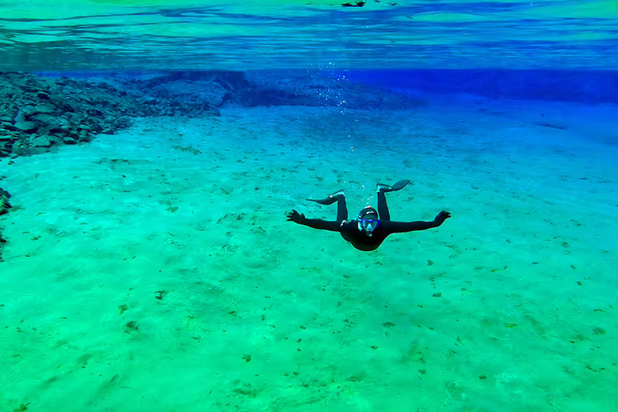 Snorkeler explores the crystal-clear waters of Silfra fissure in Iceland, highlighting unique underwater scenery on a guided tour.