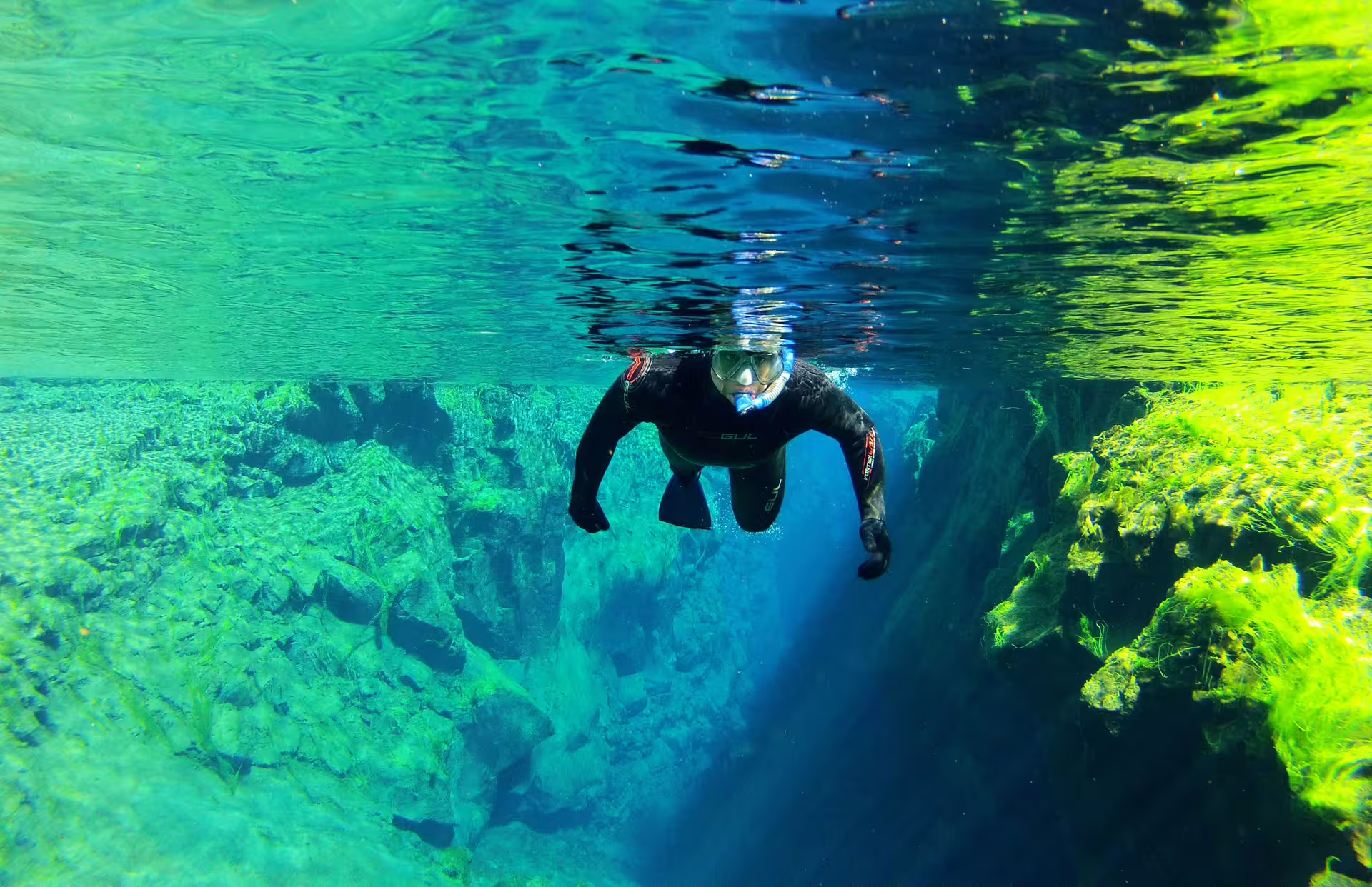 Snorkeler explores the crystal-clear waters of Silfra fissure in Iceland, surrounded by vibrant underwater scenery and rock formations.