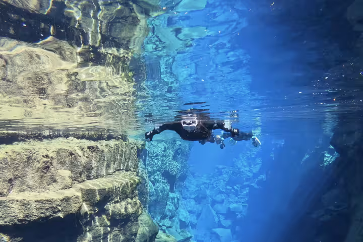 Snorkeler diving between tectonic plates in crystal clear Silfra fissure, Iceland