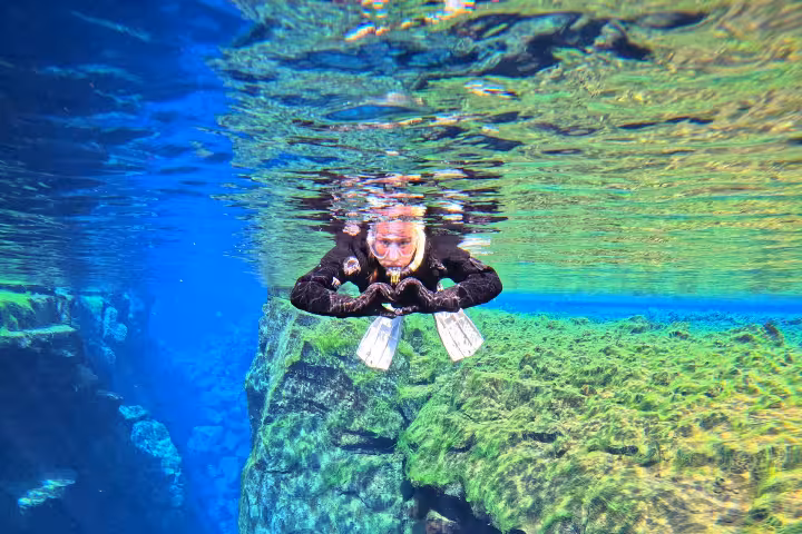 Snorkeler in black wetsuit and fins floating between tectonic plates in crystal clear Silfra fissure, Iceland