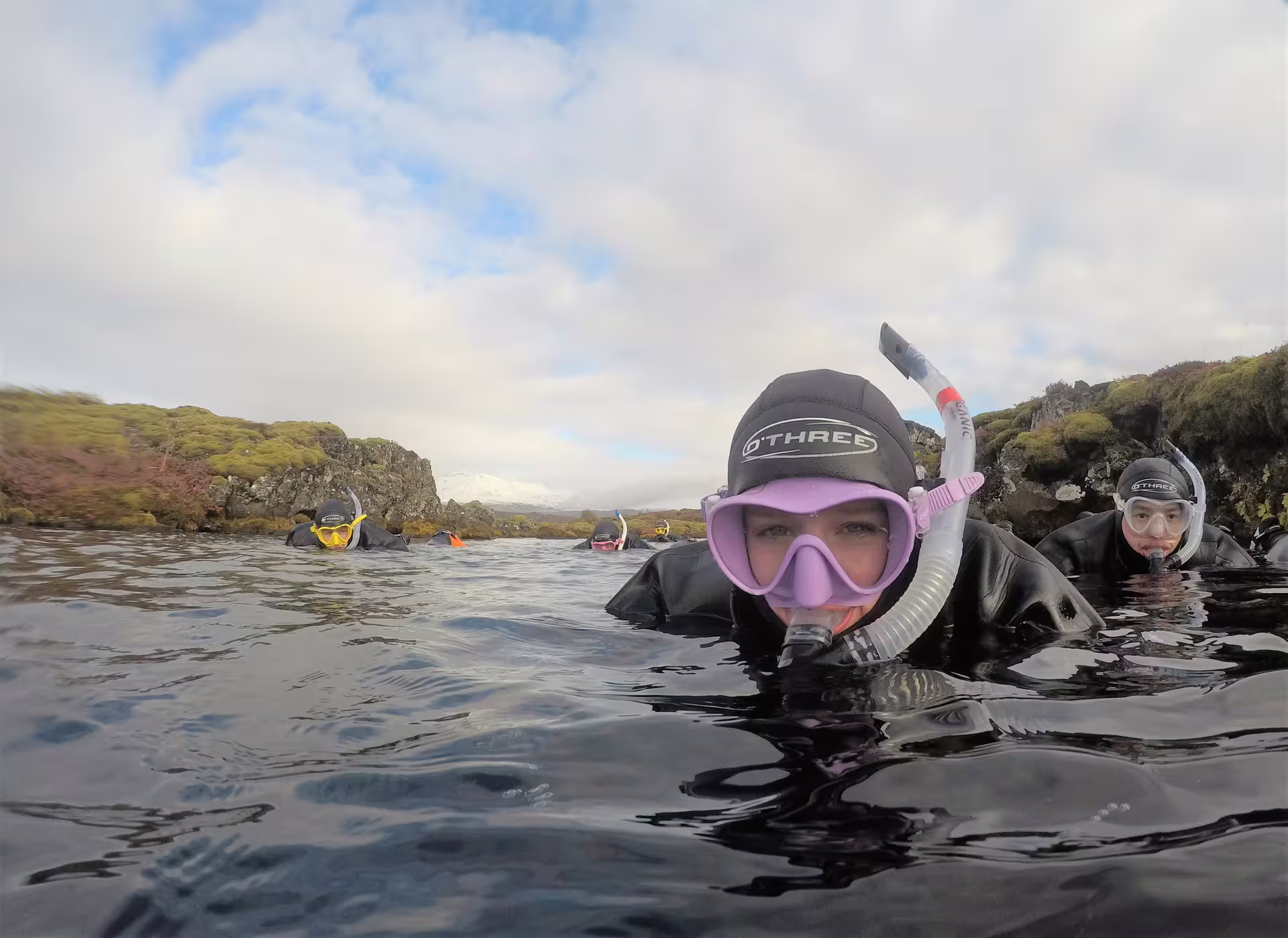 Snorkelers in wetsuits floating in Silfra fissure, Thingvellir Iceland, wearing O'Three gear and colorful masks