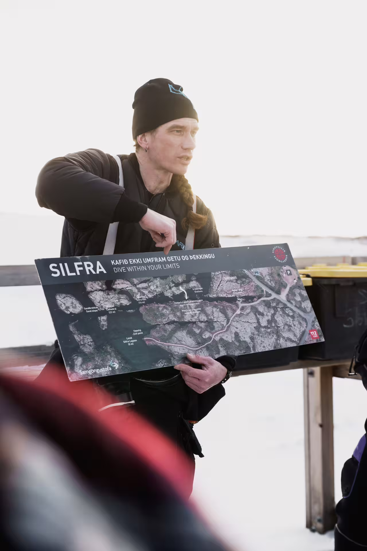 Tour guide holding a detailed Silfra snorkeling map, explaining the dive experience near Reykjavik in Iceland's clear waters.