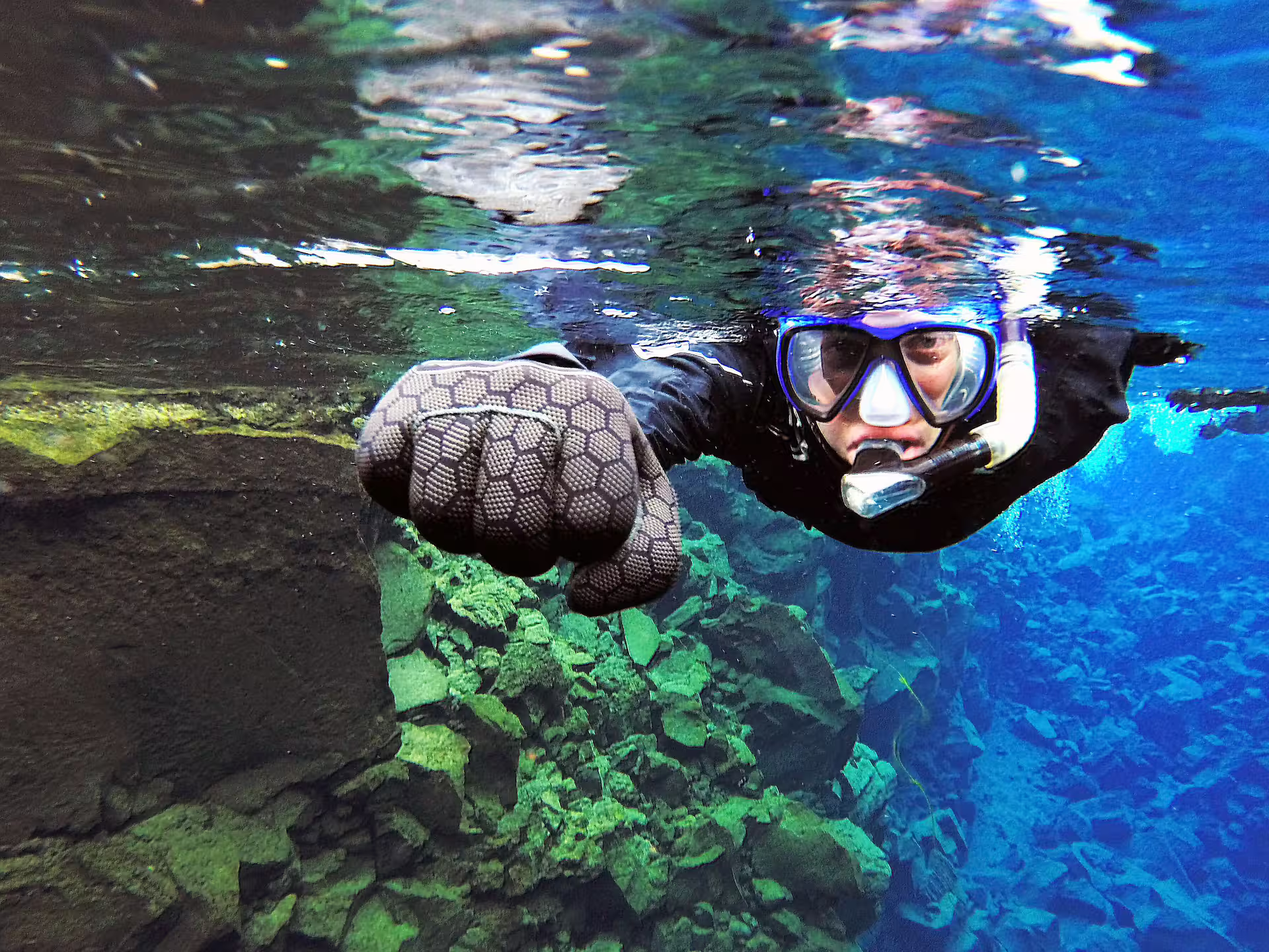 Snorkeler explores the crystal-clear waters of Silfra, surrounded by vivid underwater rock formations, capturing the adventure on camera.