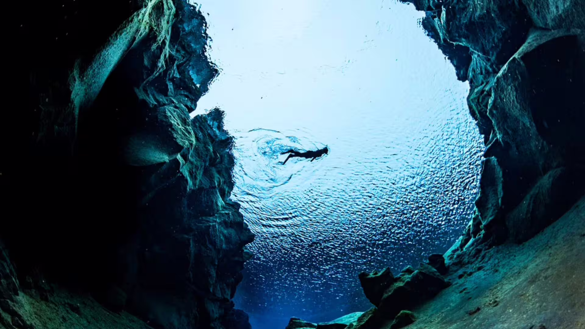 Underwater view of snorkeler at Silfra fissure Iceland with crystal clear blue water and rocky walls
