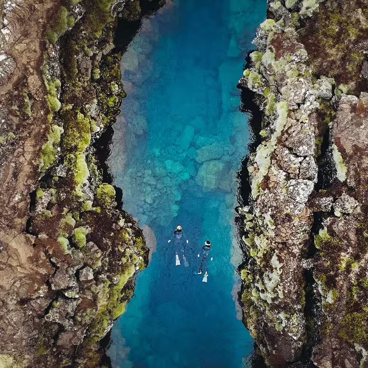 Snorkelers explore the crystal-clear waters of Silfra fissure in Iceland, surrounded by stunning volcanic rock formations.