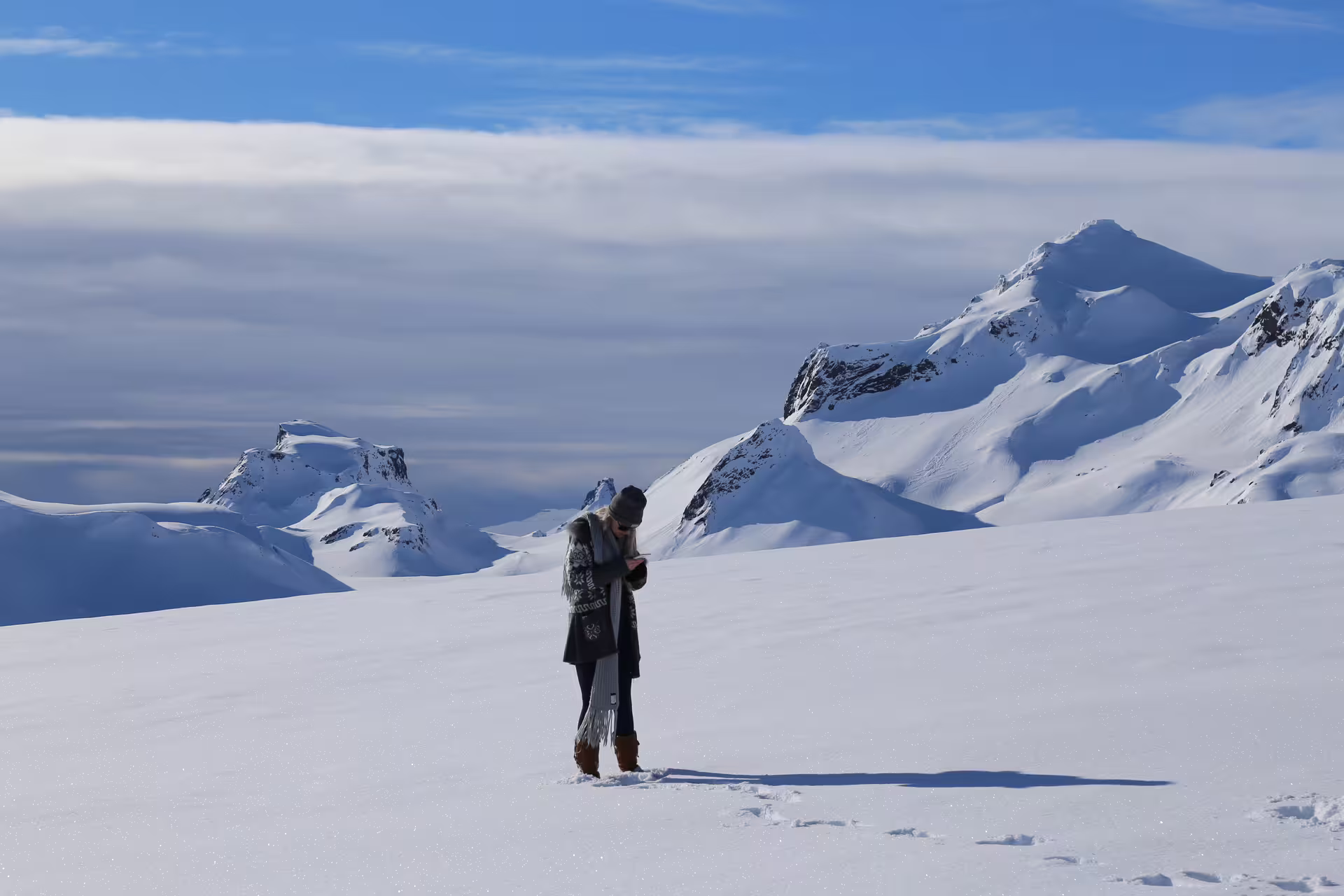 Person standing on a snowy landscape with majestic mountains in the background during Silfra Superjeep Golden Circle tour.