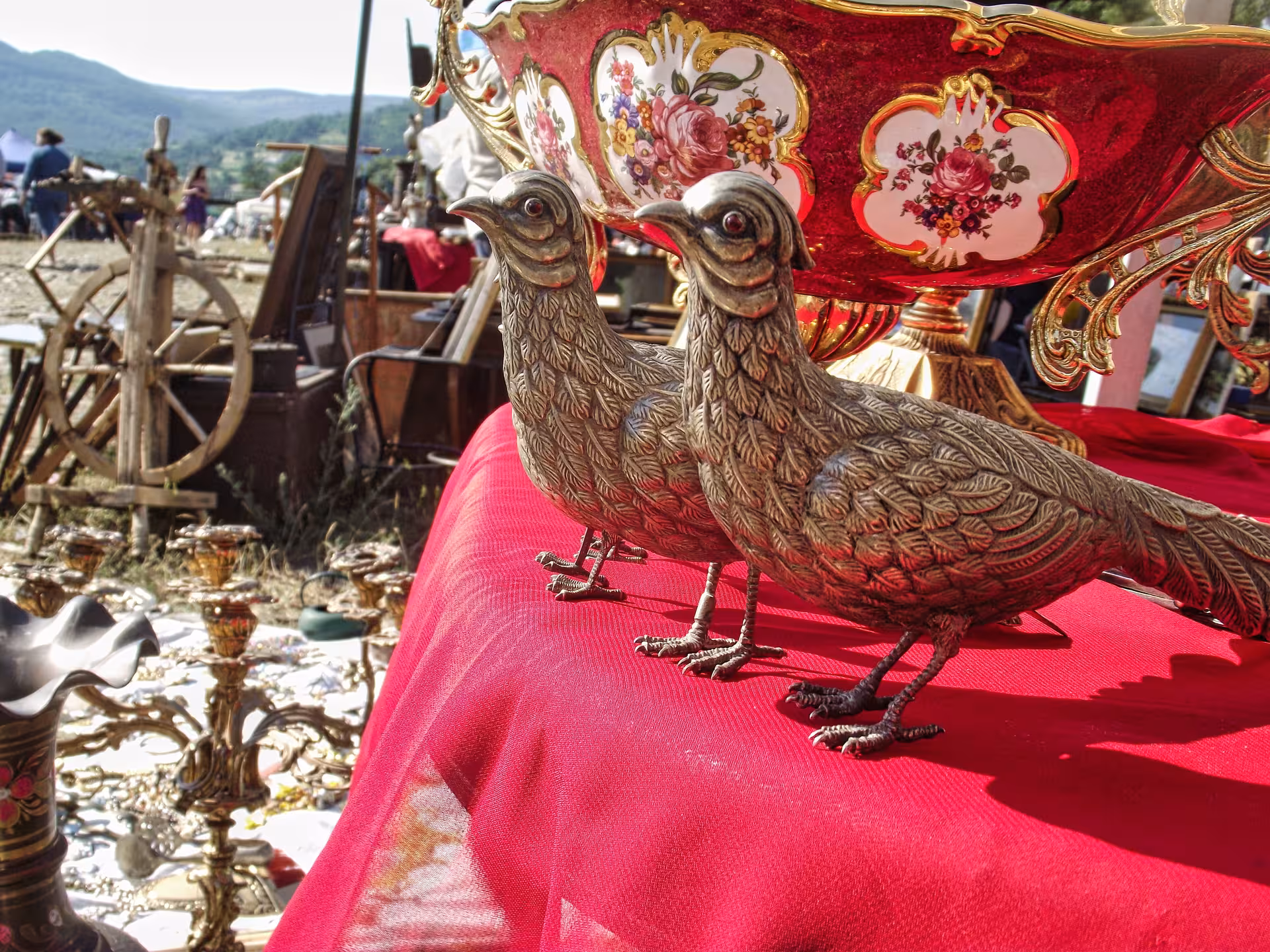 Ornate silver bird figurines and red floral porcelain antiques displayed at Negreni Flea Market guided tour Romania