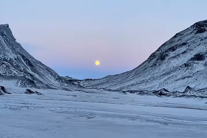 Full moon rising between snow-covered mountains in a vast winter valley near Reykjavik, Iceland