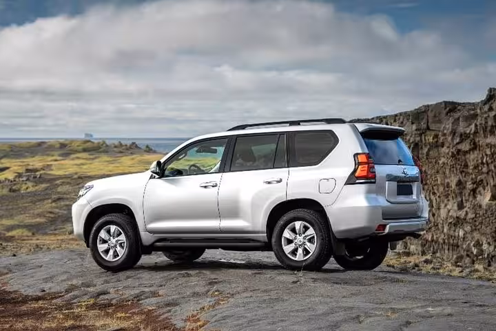 Silver Toyota Land Cruiser Prado SUV parked on rocky Icelandic landscape with cloudy sky