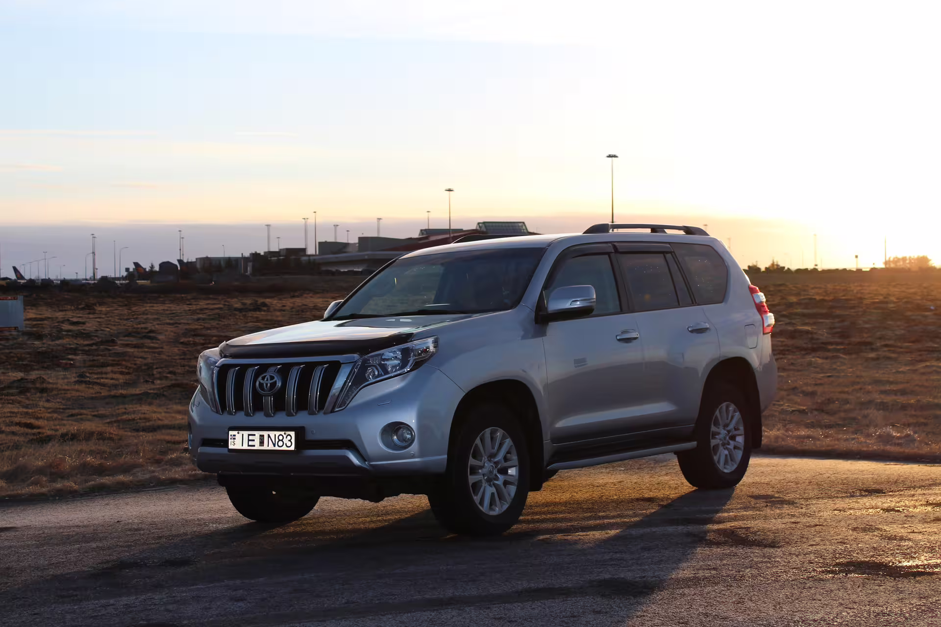 Silver Toyota Land Cruiser Prado SUV parked near airport at sunset for private transfer service