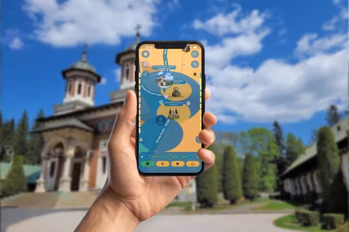 Hand holding smartphone with self-guided tour app at Sinaia Monastery, Romania