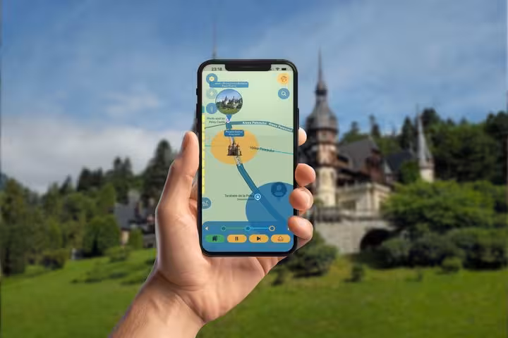 Hand holding smartphone with self-guided tour app map in front of Peles Castle in Sinaia, Romania