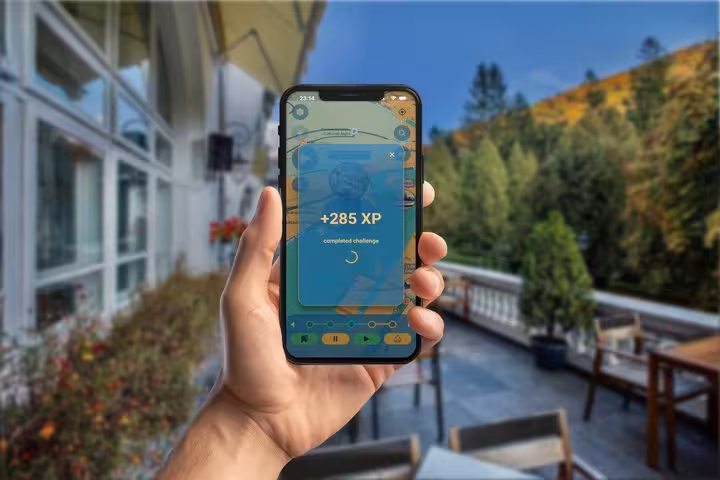 Hand holding smartphone displaying +285 XP challenge completion screen on self-guided walking tour app in Sinaia