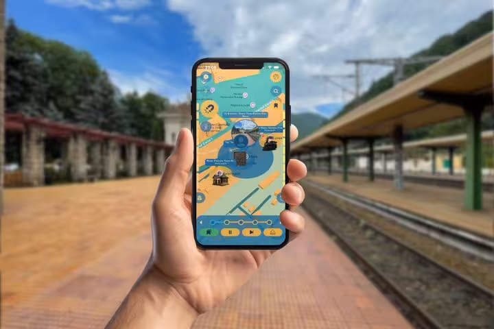 Hand holding smartphone displaying self-guided walking tour map app at Sinaia train station platform