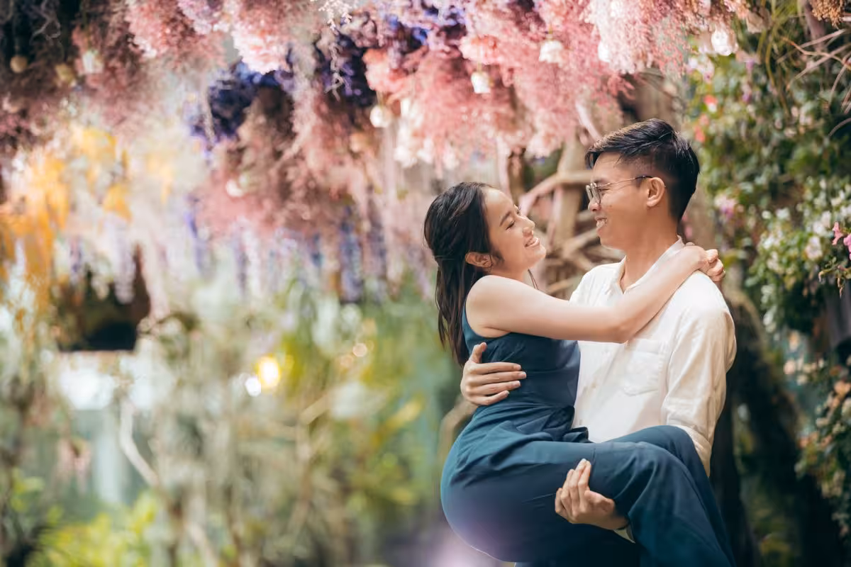 Man joyfully lifts woman under colorful floral canopy, capturing romance on a Singapore private photoshoot.