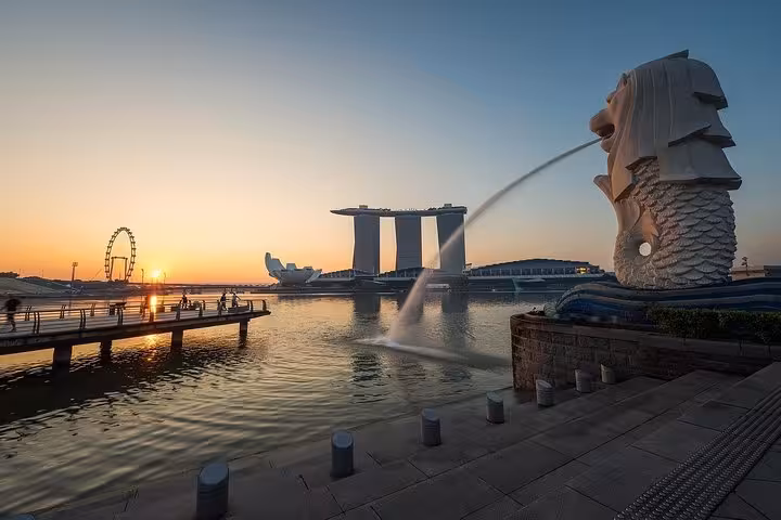 Iconic Merlion statue spouting water at sunrise with Marina Bay Sands and Singapore Flyer in background