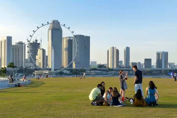 Tourists relaxing on green lawn with Singapore Flyer and city skyline during 8-hour private car tour