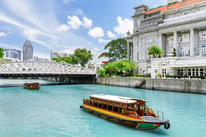 Colorful bumboat cruising Singapore River past Cavenagh Bridge and colonial Fullerton Hotel