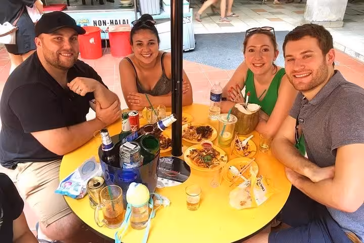 Group enjoying traditional Singaporean street food and drinks at an outdoor table during a cultural tour.