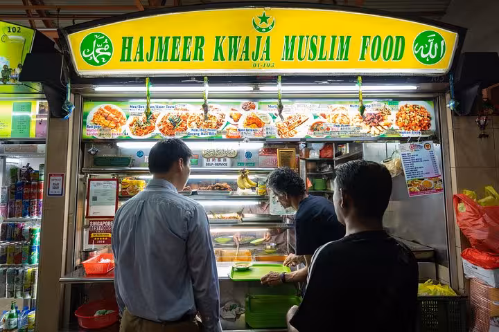 Visitors enjoying traditional dishes at Hajmeer Kwaja Muslim Food stall in Singapore's vibrant street food scene.