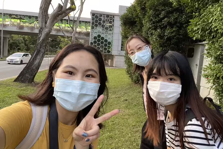 Three women wearing face masks taking a selfie outdoors near a modern building in Singapore