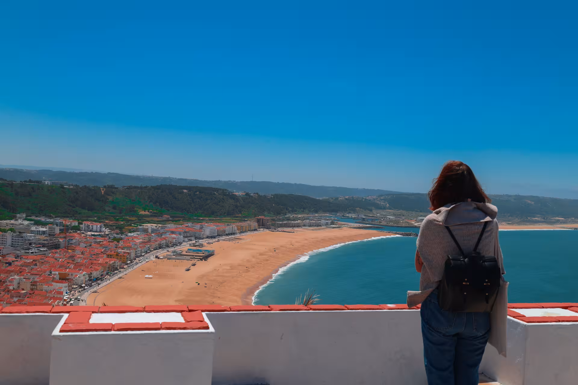 Woman enjoying panoramic view of coastal town and sandy beach from a scenic vantage point near Lisbon.