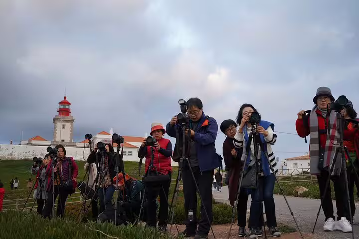 Tourists with cameras capture scenic views near the historic lighthouse on a half-day Sintra sightseeing tour from Lisbon.