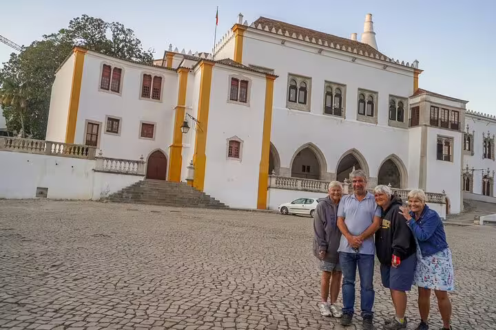 Tourists enjoy a Sintra half-day sightseeing tour, standing in front of the historic National Palace of Sintra in Portugal.