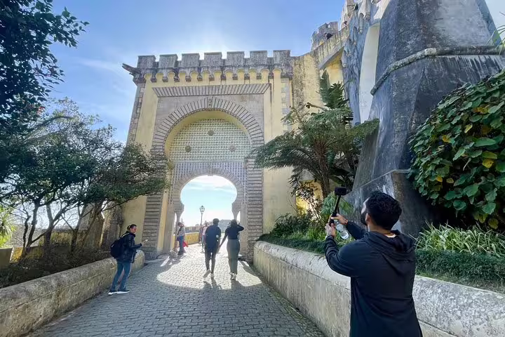 Visitors explore the historic entrance of a castle in Sintra, surrounded by lush greenery, on a private tour with wine tasting.