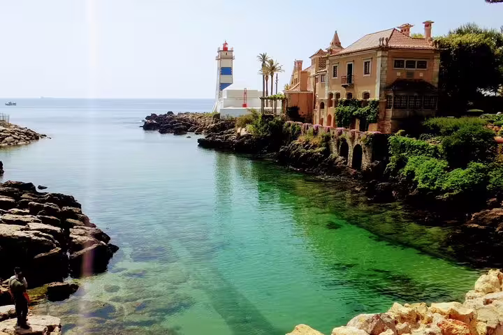 Scenic view of a picturesque coastal village near Sintra with a lighthouse, charming villa, and crystal-clear waters.