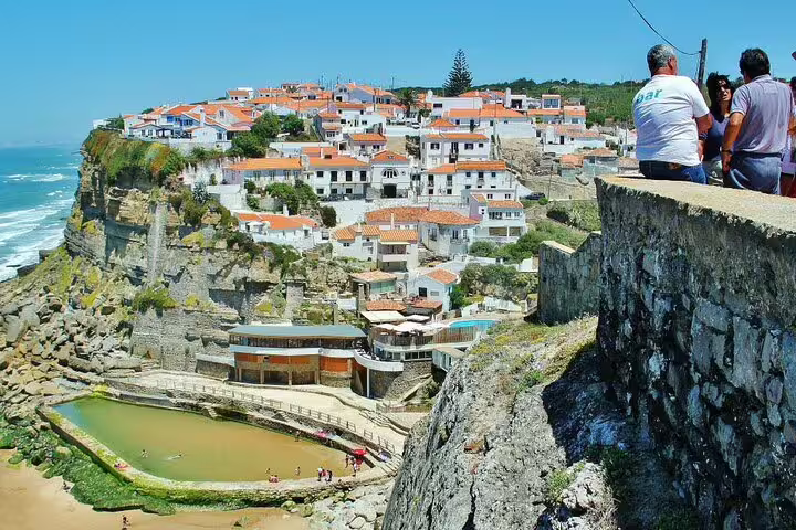 Scenic view of Sintra's coastal village with whitewashed houses and tourists enjoying the stunning ocean vista.