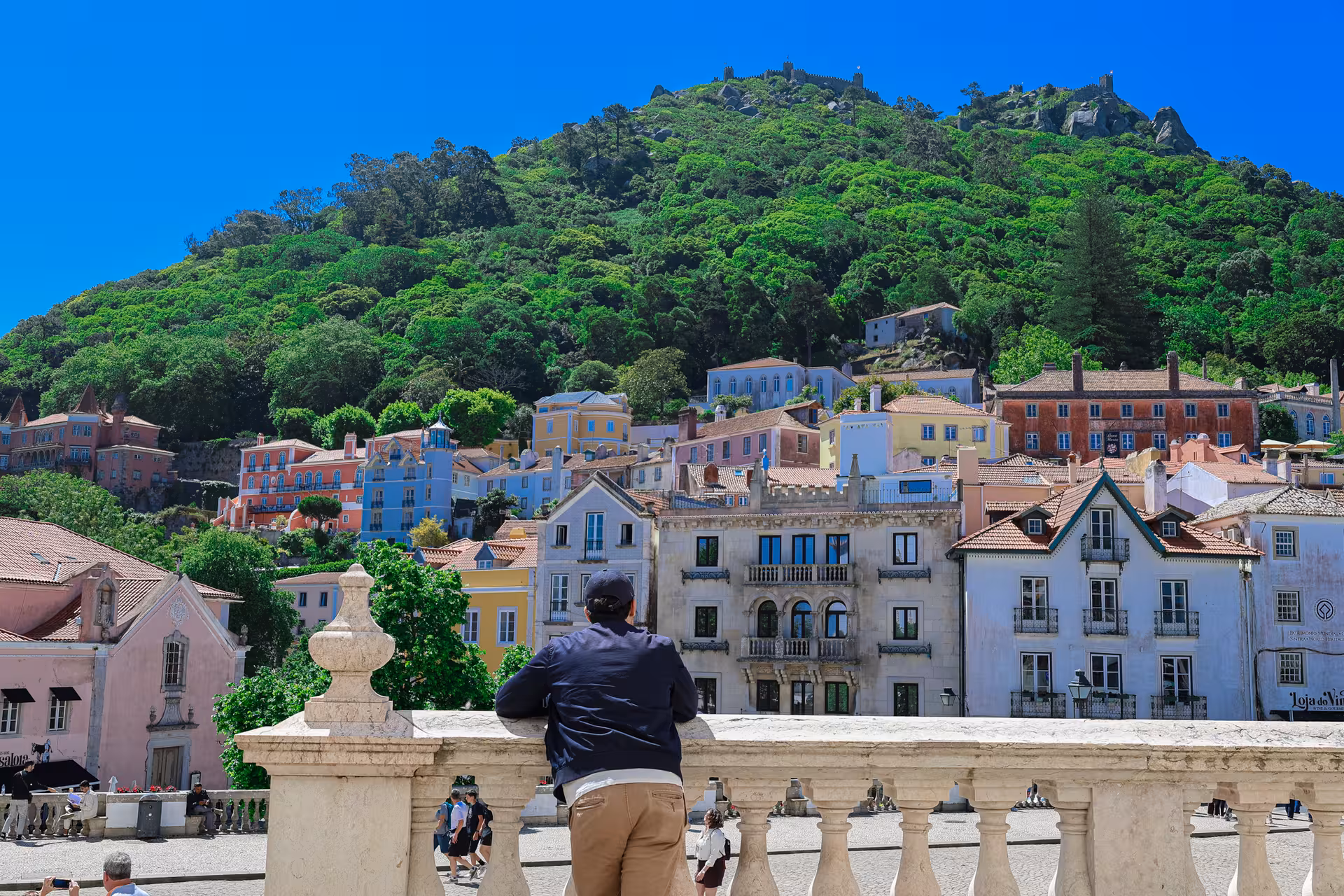 Visitor enjoys vibrant hillside view of colorful Sintra houses on a sunny day during Lisbon small group tour.