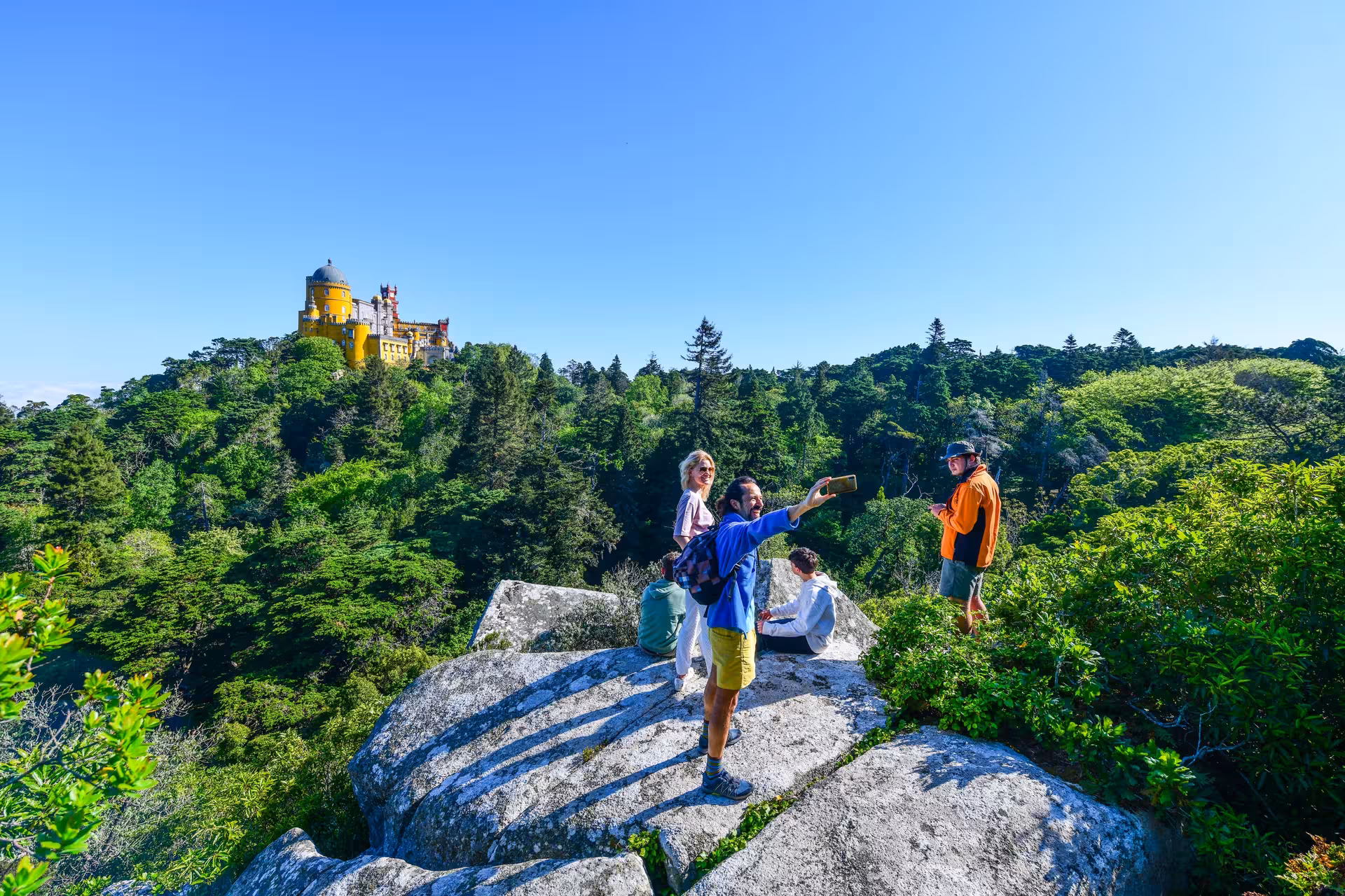 Tourists enjoying a scenic view of Pena Palace from a rocky Sintra hilltop during the 5 Senses e-Bike Tour.