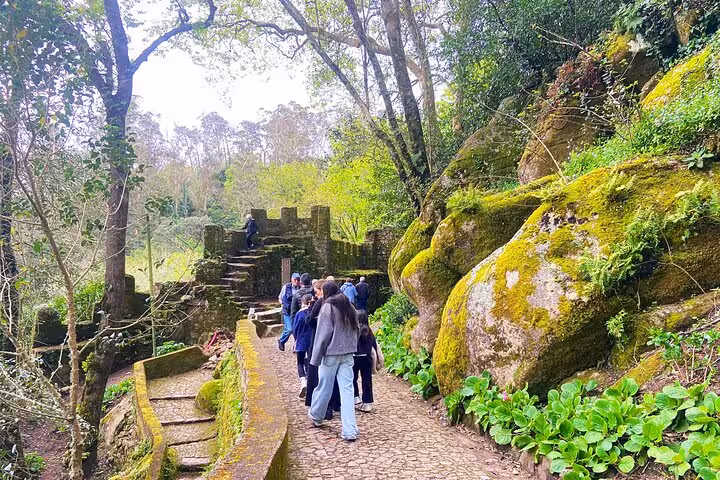 Group walking mossy stone path in Sintra forest, tuk tuk tour stop near castles and hidden trails